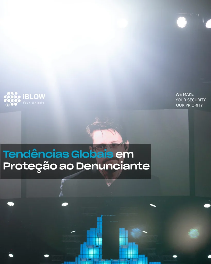 Imagem, em 3 ecrãs gigantes, de um dos mais famosos denunciantes, usando óculos e vestido de fato preto com uns headphones internos com fio, com o nome de Edward Snowden.